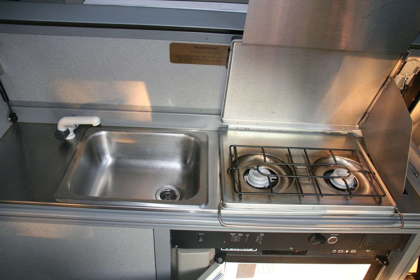 This RV rental's compact kitchen features a stainless steel sink, a two-burner gas stovetop, and a control panel for convenience.