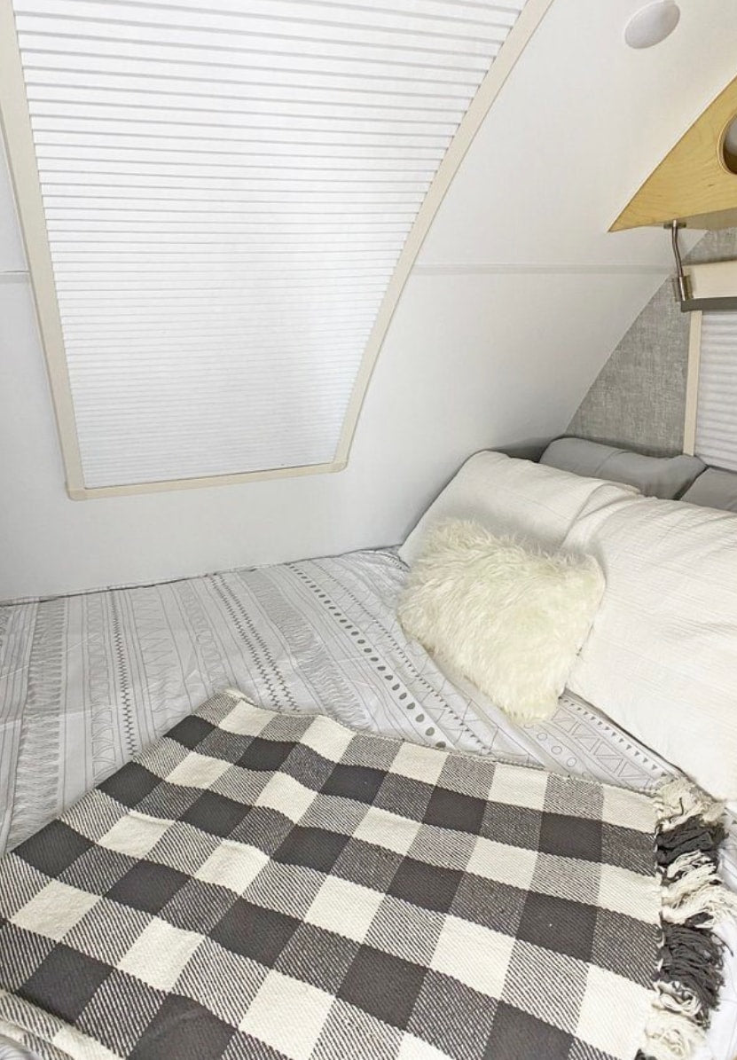 Cozy RV rental bedroom with white bedding, a fluffy pillow, and black & white plaid blanket.