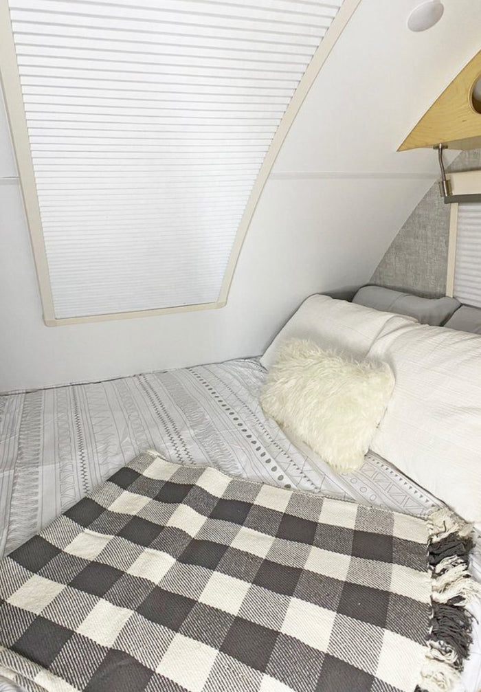 Cozy RV rental bedroom with white bedding, a fluffy pillow, and black & white plaid blanket.