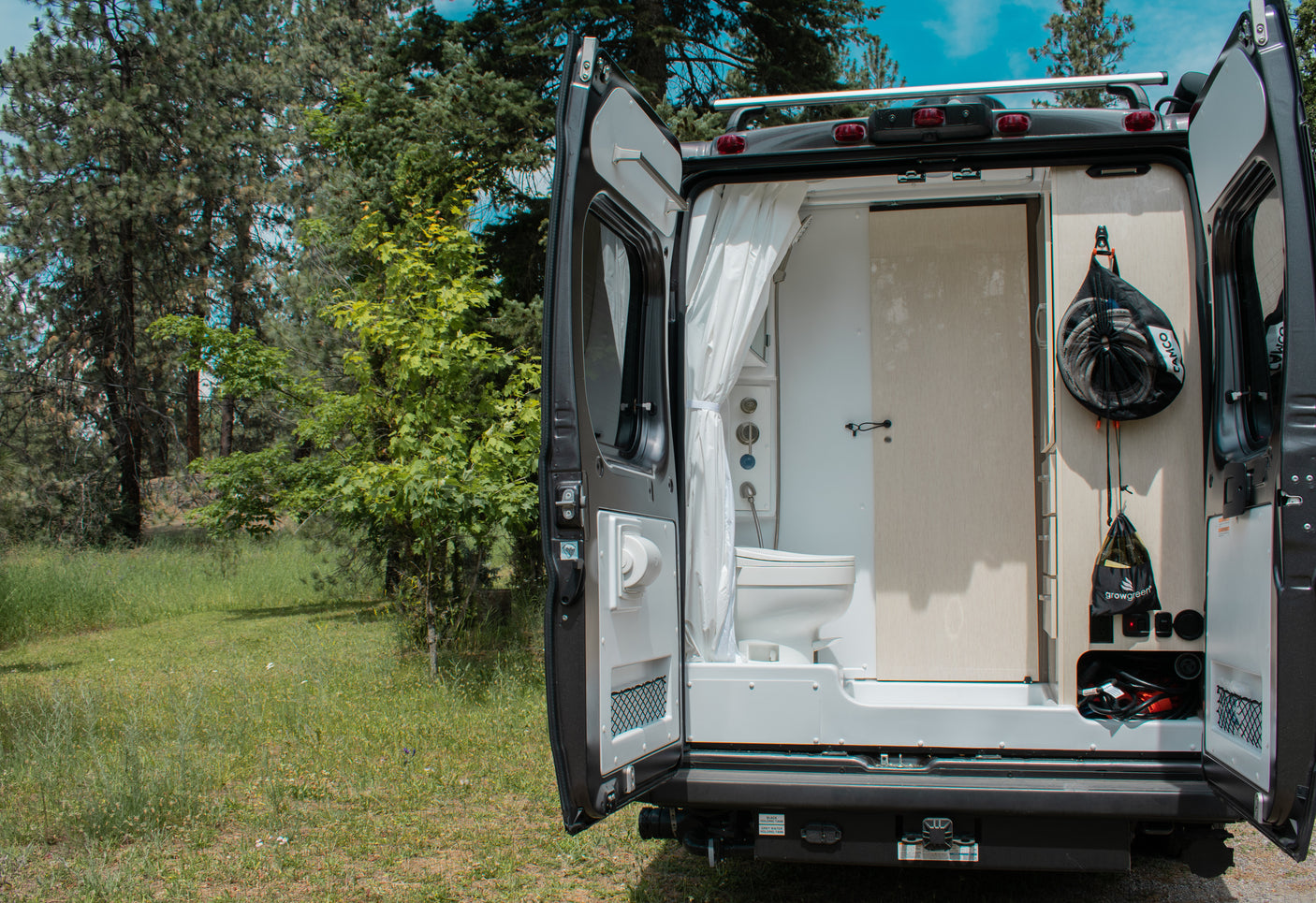 RV rental van's open rear doors show a compact shower, toilet, and utility storage. Ready for your next outdoor adventure.
