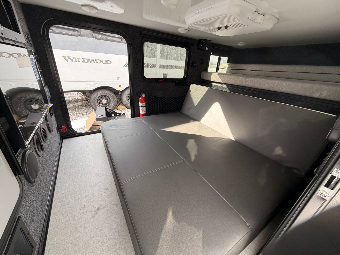 Inviting rv rental interior: large gray bed/couch, light carpet, AC, and bunks. Ready for your camping journey.
