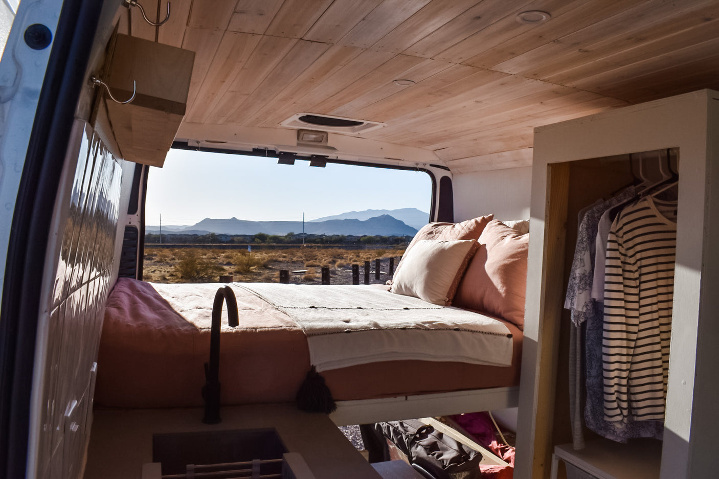 RV rental interior: cozy bed, kitchen, and closet, with a stunning desert mountain view from the open rear doors.