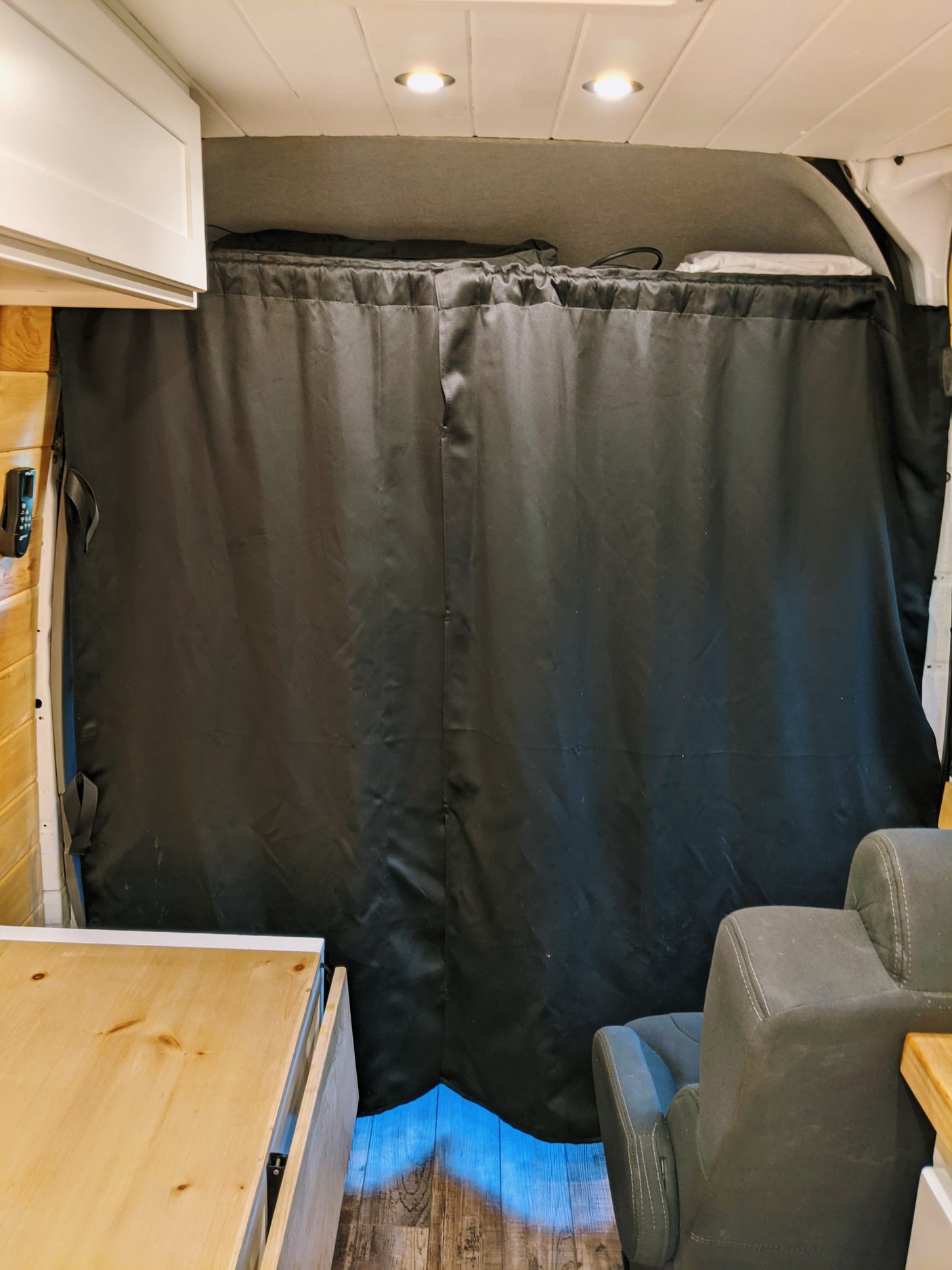 RV rental interior. A large black privacy curtain separates the rear, complemented by white cabinets, wood paneling, and a grey seat.