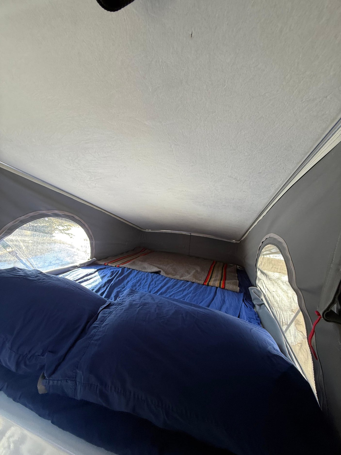 RV rental pop-top interior: a cozy bed with blue bedding and a striped blanket, illuminated by side windows.
