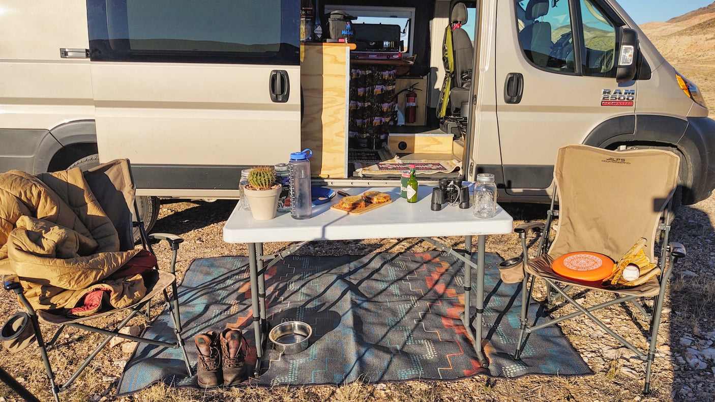 RV rental van life: Converted van with outdoor camp setup. Table, chairs, food, gear & dog bowl for a desert adventure.
