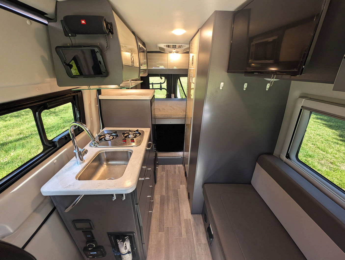 Modern RV rental interior: kitchen with sink & stove, lounge seating, and rear sleeping area.
