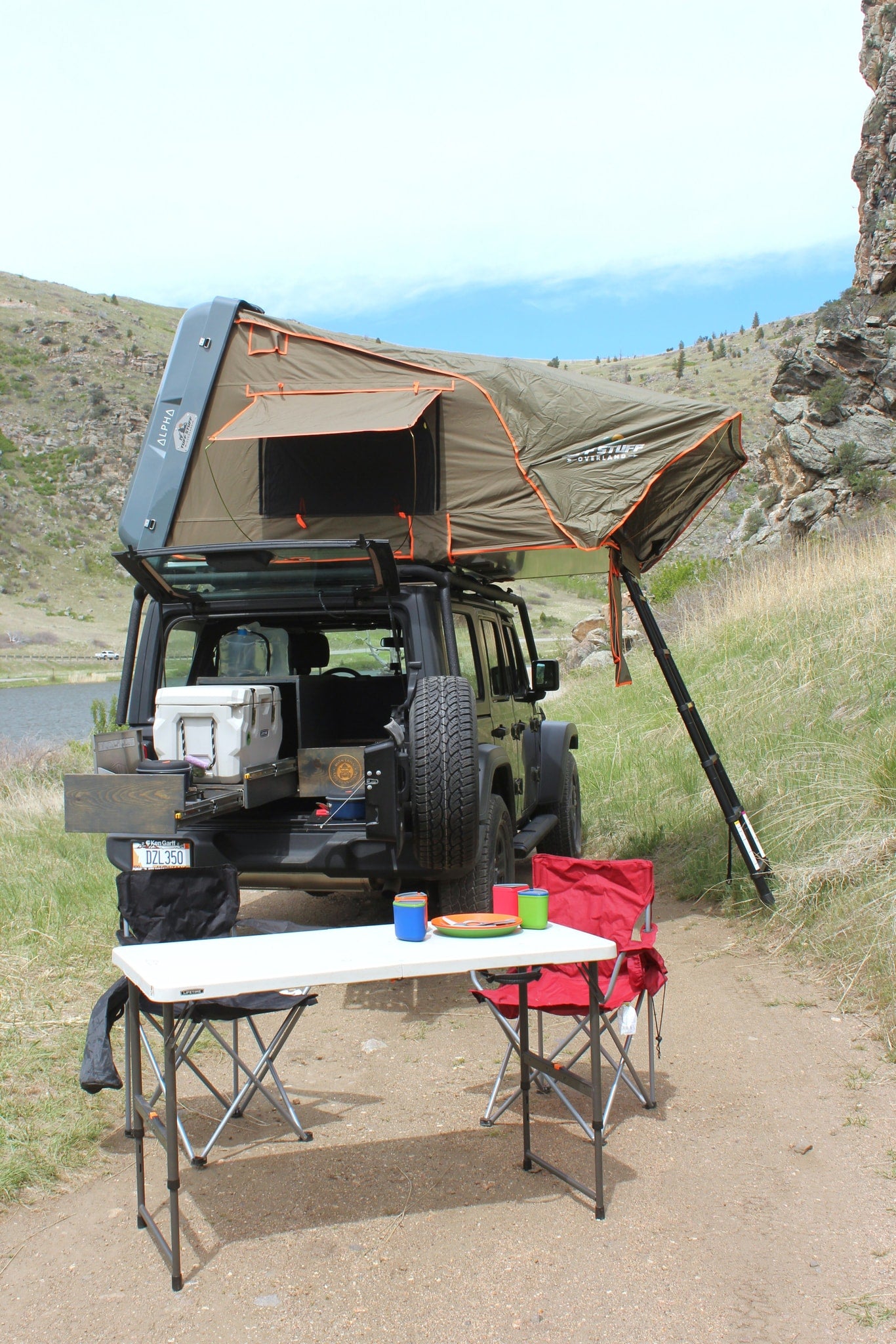 An overland Jeep with a deployed rooftop tent and camp setup is parked by a lake. Ideal for adventure travel as an RV rental alternative. — photo 3