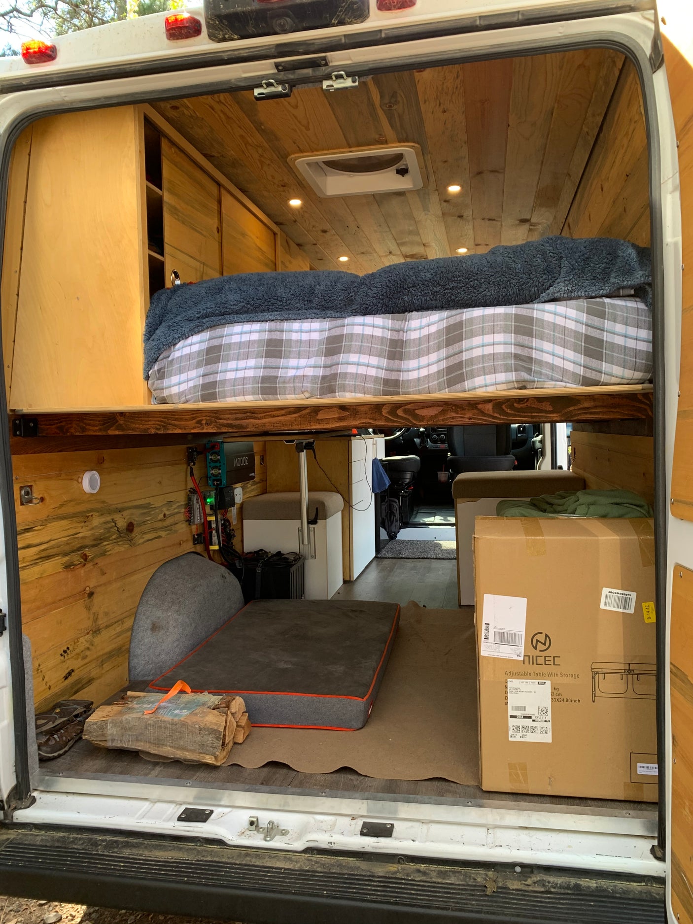 Inside this cozy RV rental: a wooden interior with a raised bed, visible power setup, and an adjustable table in its box, ready for use.