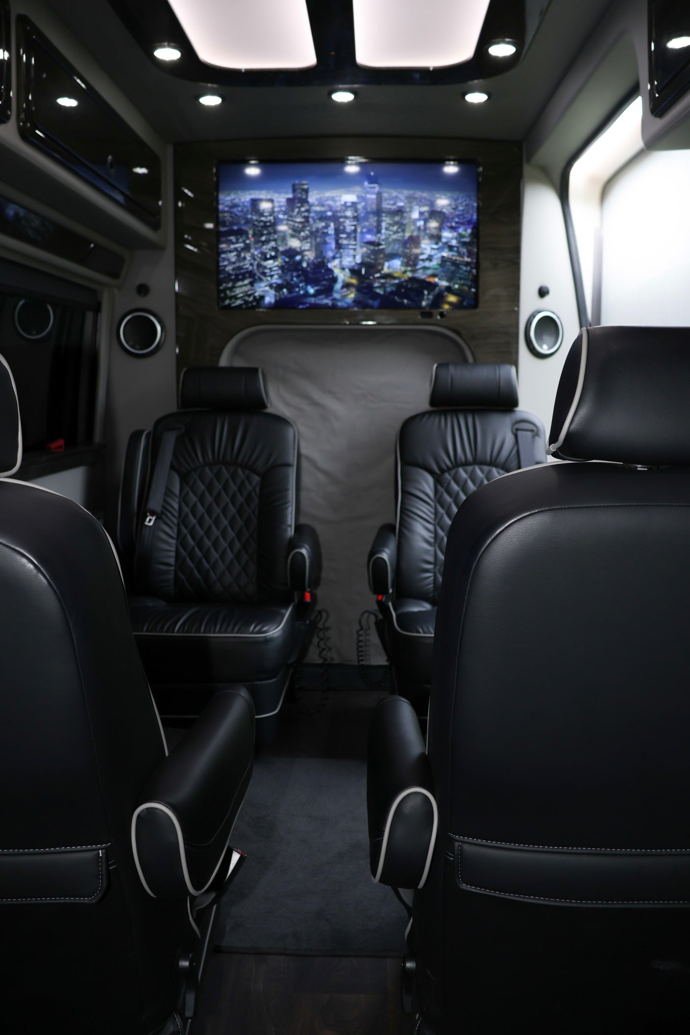 Luxury RV rental interior: black leather captain's chairs, a large TV displaying a cityscape, and mood lighting for comfort.