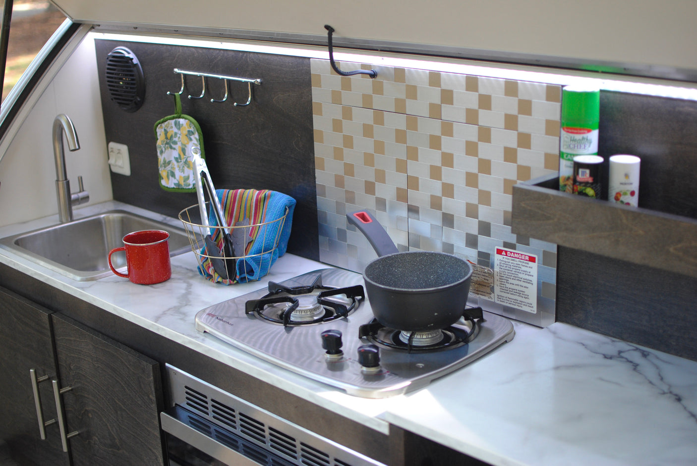 An RV rental kitchenette features a sink, two-burner stove with a pot, and counter space for compact travel cooking.