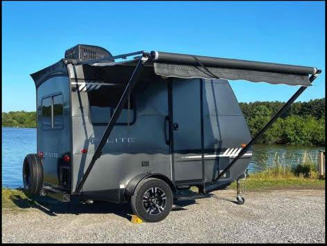 perfect for an RV rental. This compact RV offers lakeside camping and adventure.|Gray teardrop RV rental with awning extended by a lake
