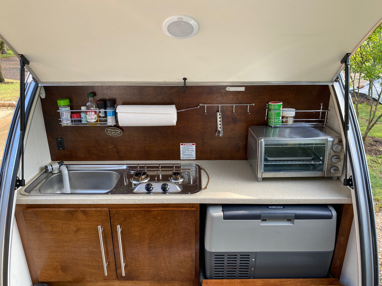 Compact RV rental outdoor kitchen with sink, stove, toaster oven, and portable fridge.