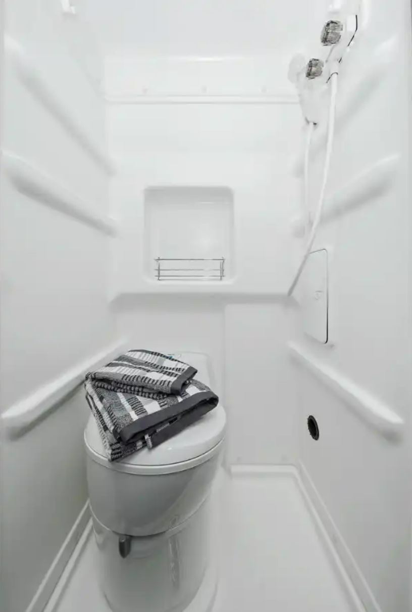 Inside an RV rental: a compact white wet bath featuring a toilet, shower, and folded towel.