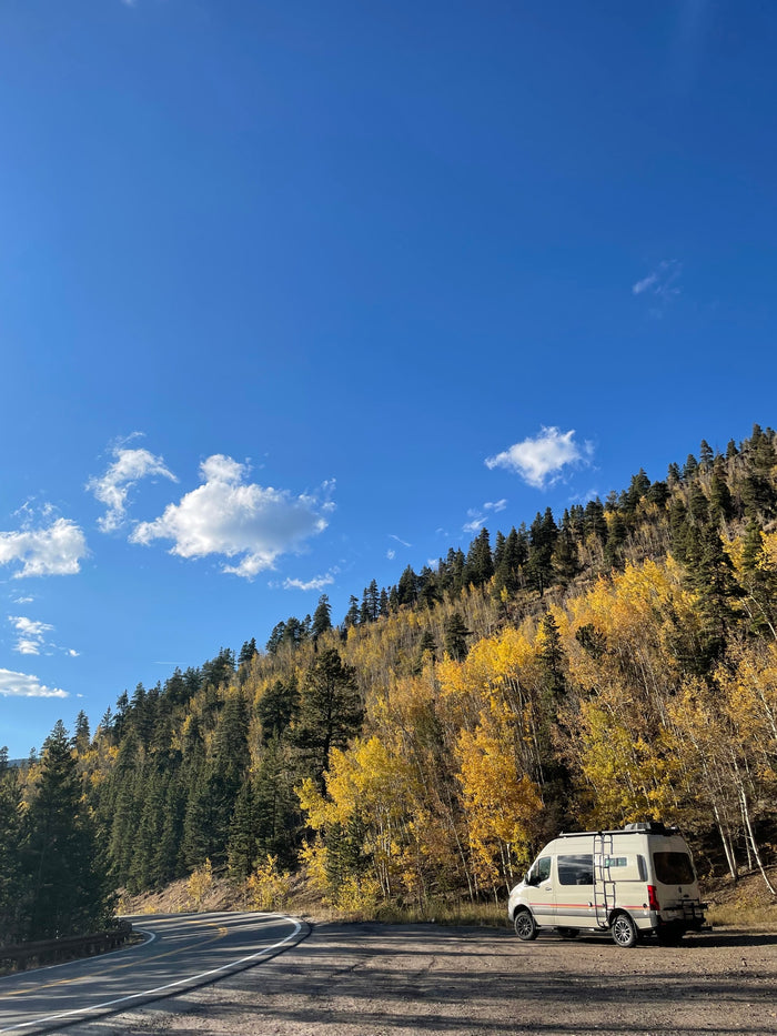 nestled among bright yellow autumn aspens and green pines under a blue sky.|Inside a cozy RV rental: a plush bed