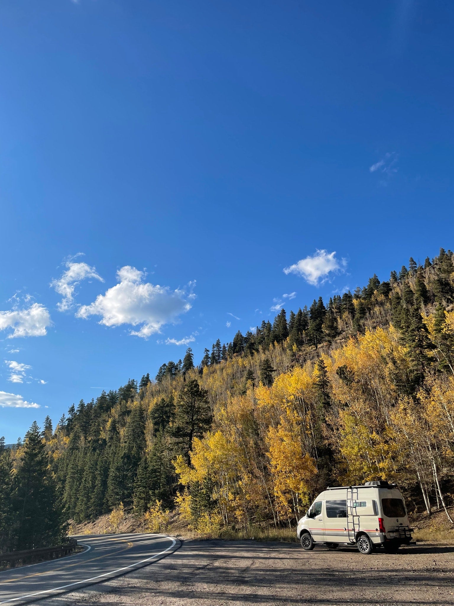 nestled among bright yellow autumn aspens and green pines under a blue sky.|Inside a cozy RV rental: a plush bed