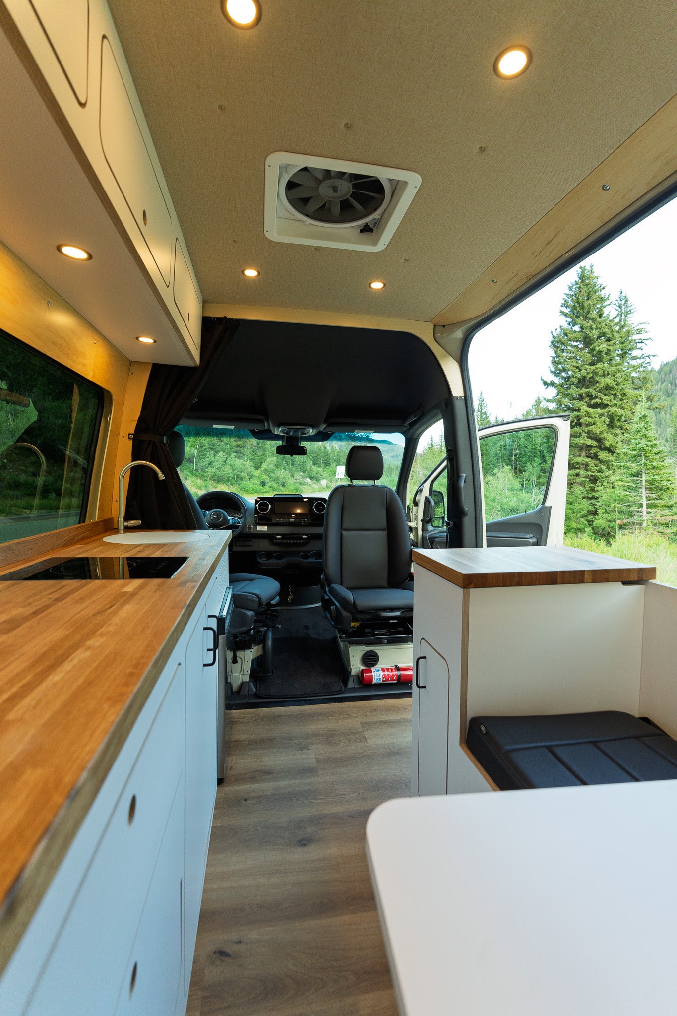 Spacious RV rental interior with a bright kitchen, wood flooring, and cozy seating looking out to nature.