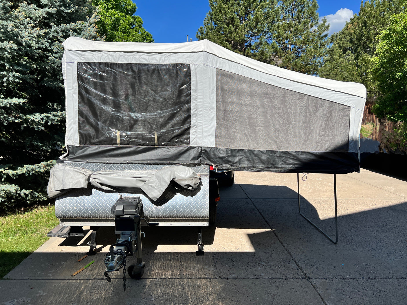 A modern pop-up camper RV rental ready for adventure, parked on a sunlit driveway amidst lush trees.