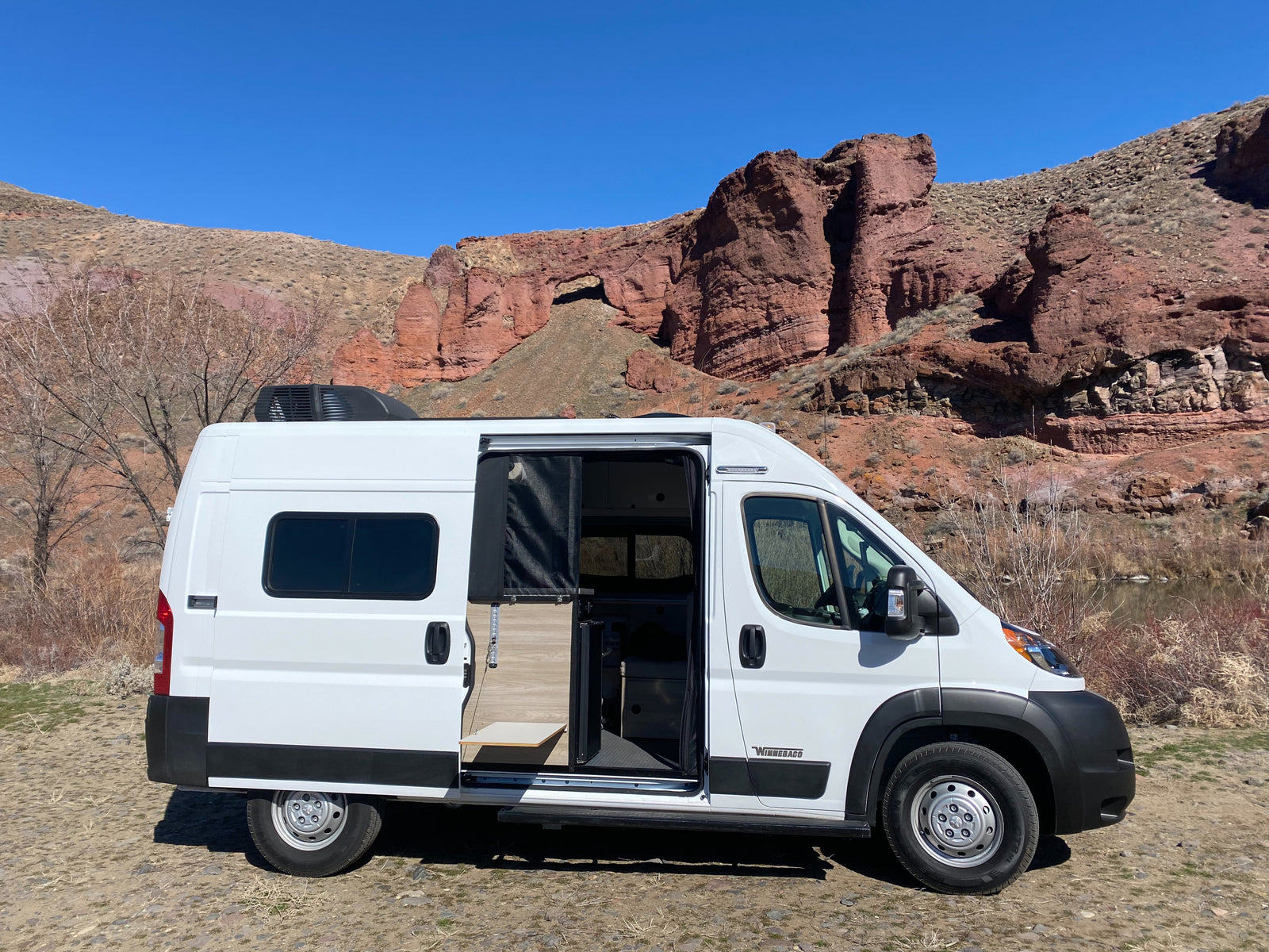 White camper van **rv rental** parked with open door revealing interior, set against stunning red rock formations & clear blue sky.