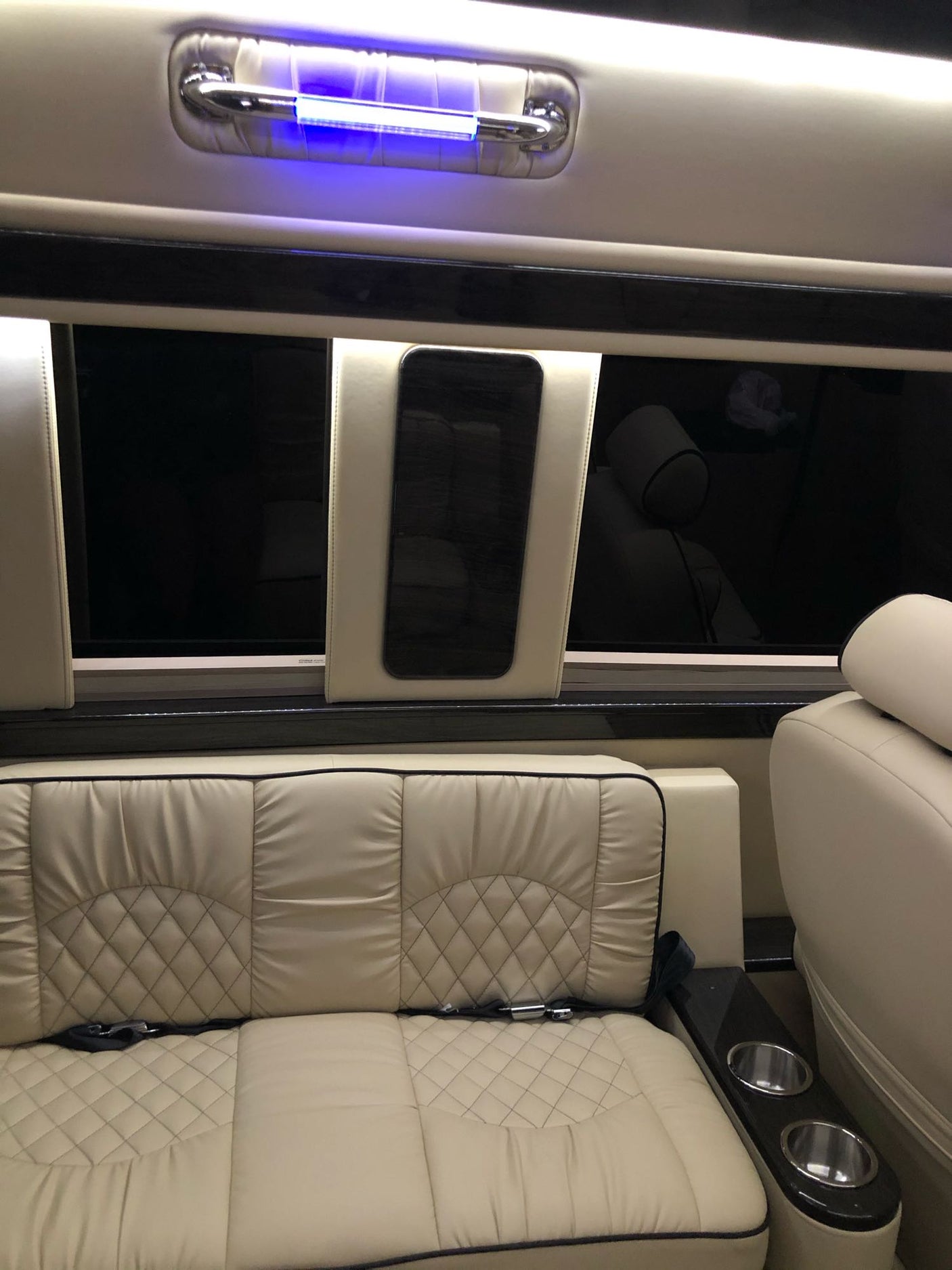 Plush cream leather interior of an RV rental, featuring diamond-stitched seating, cup holders, and overhead blue lighting for comfortable travel.