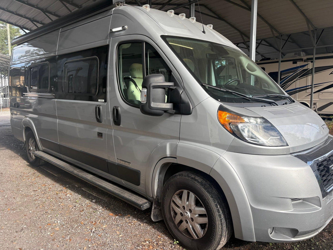 Silver campervan RV rental parked under a shelter. This modern motorhome is ready for a comfortable road trip adventure.|Silver Winnebago Travato rv rental — photo 1