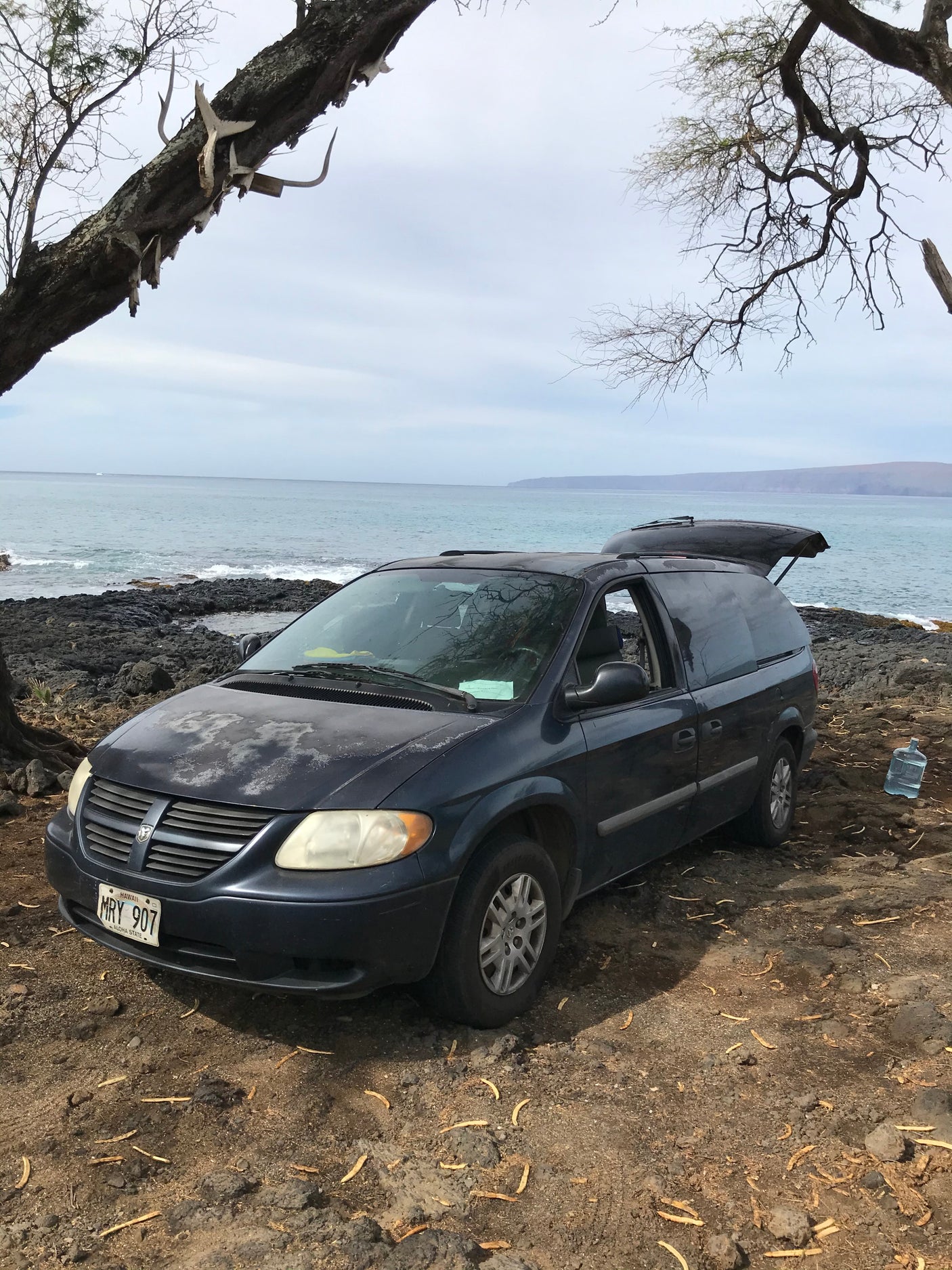 Ocean camping in Hawaii: a dark blue Dodge Caravan (open hatch), a practical RV rental choice.