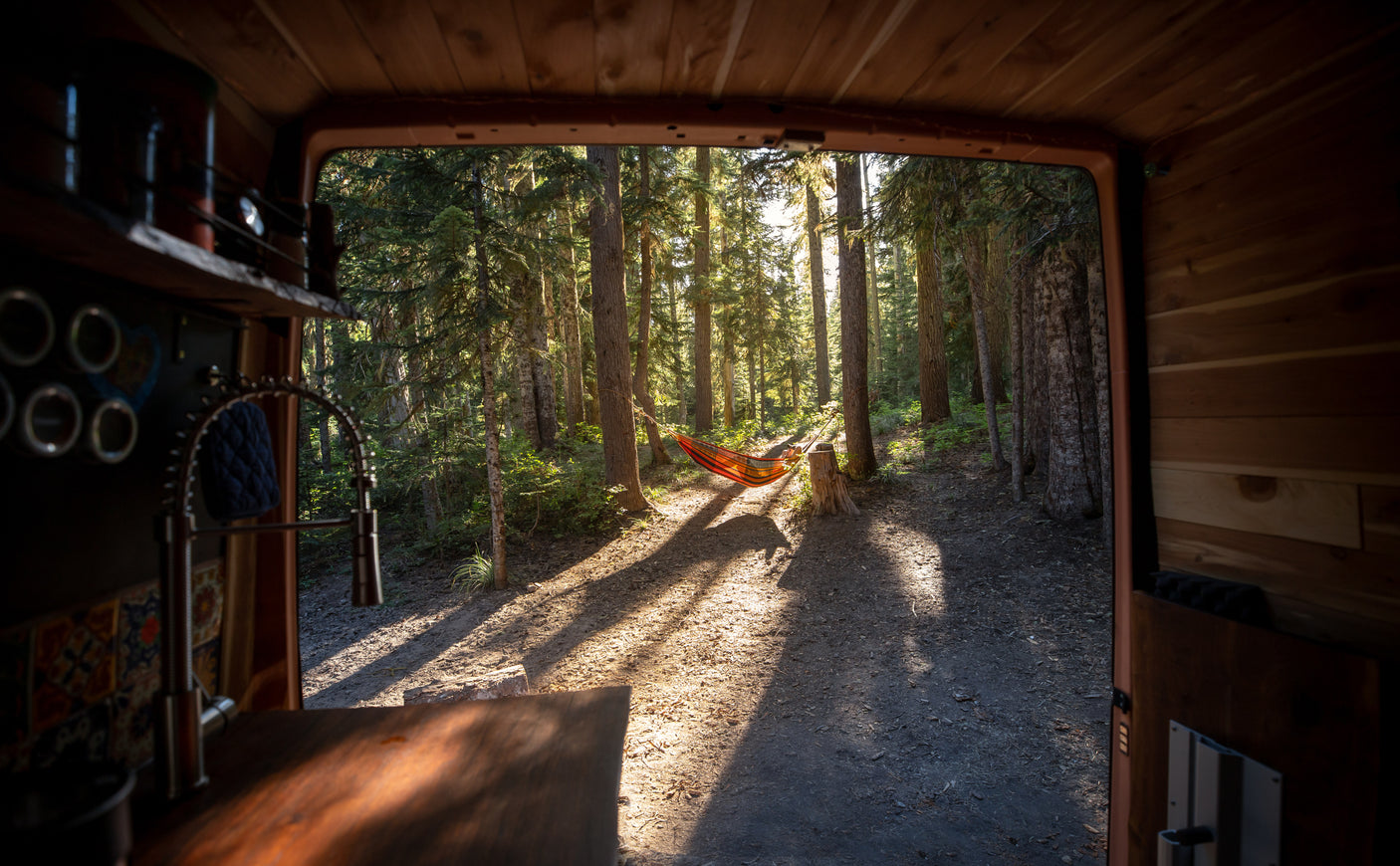 View from an RV rental: a forest scene with a person relaxing in a sunlit hammock. Interior elements visible.