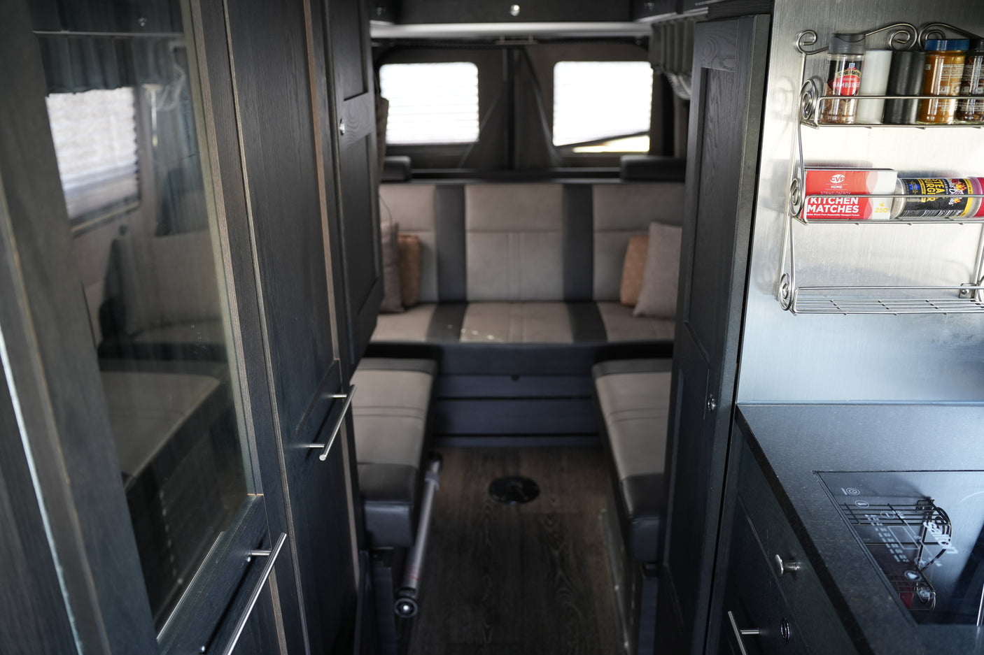 Modern rv rental interior: dark wood cabinets, plush gray seating, and a compact kitchen with a spice rack and stovetop.