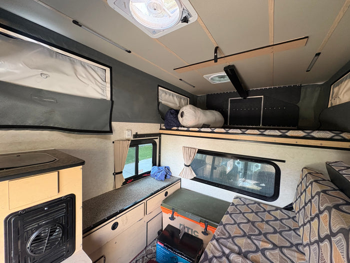 Explore this cozy RV rental interior: kitchenette, sleeping bunk, and comfortable seating for your next adventure.