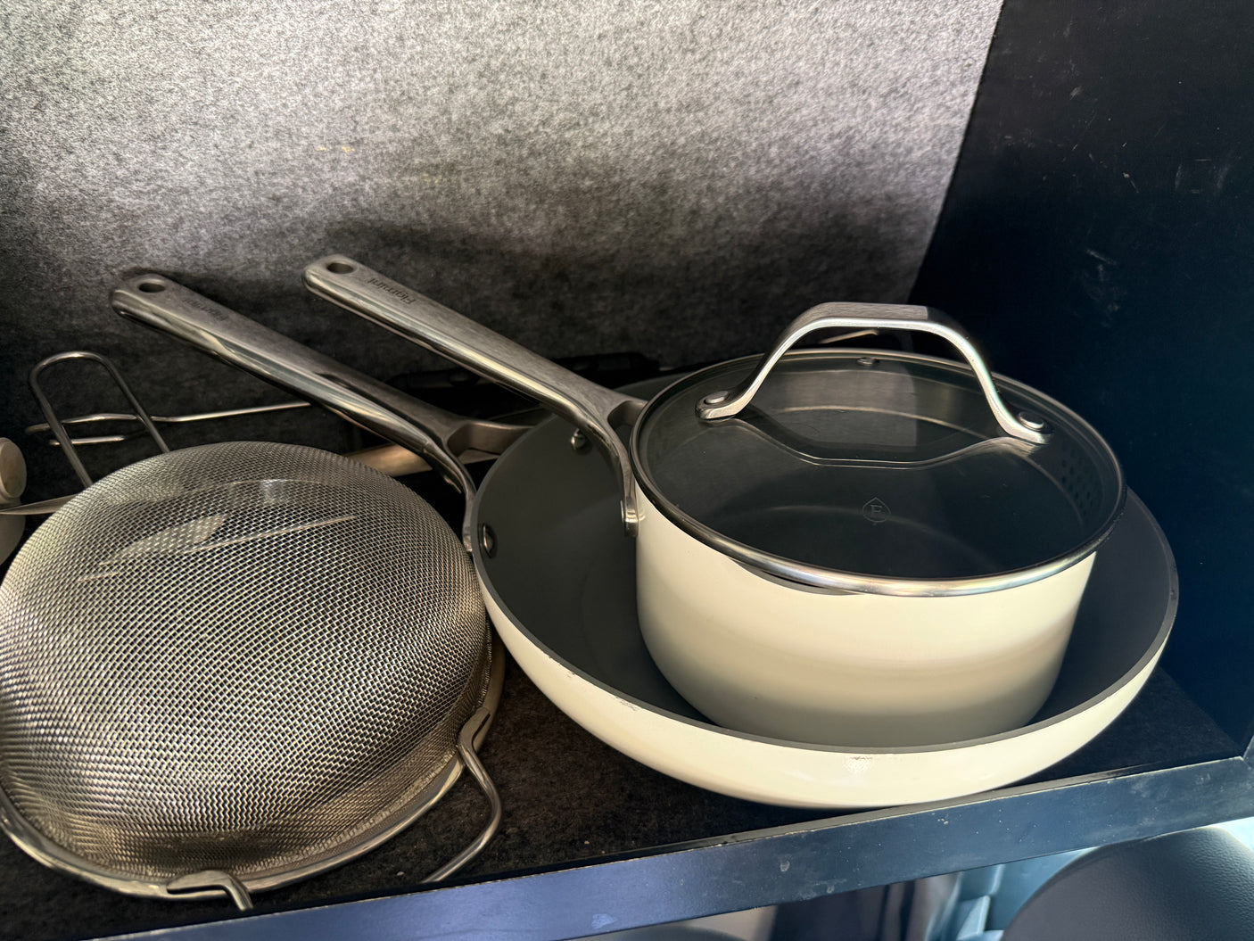 RV rental kitchen gear: beige saucepan with lid, frying pan, and a metal colander, neatly stored.