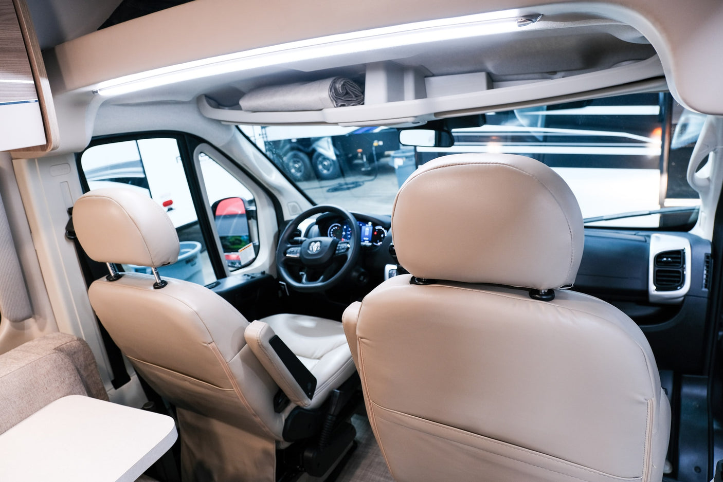Inside a clean RV rental: Front cabin view with comfortable light-colored seats, steering wheel, and overhead storage.
