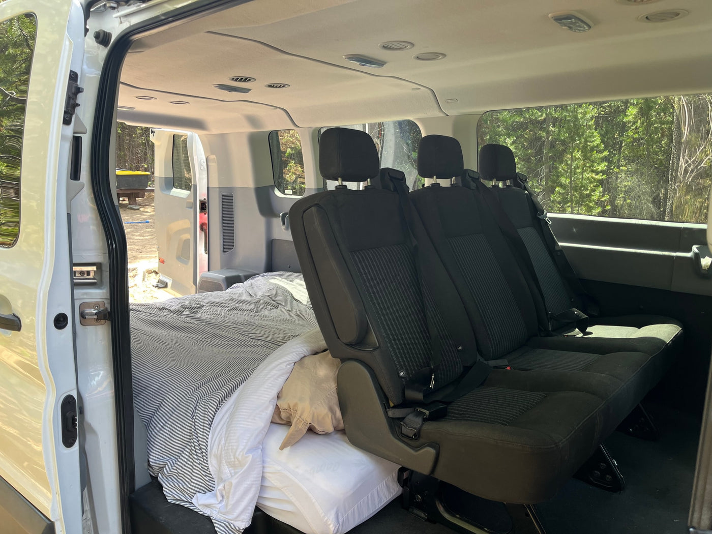 RV rental van interior shows a convertible space with a bed on one side and passenger seats on the other for adaptable travel. — photo 11