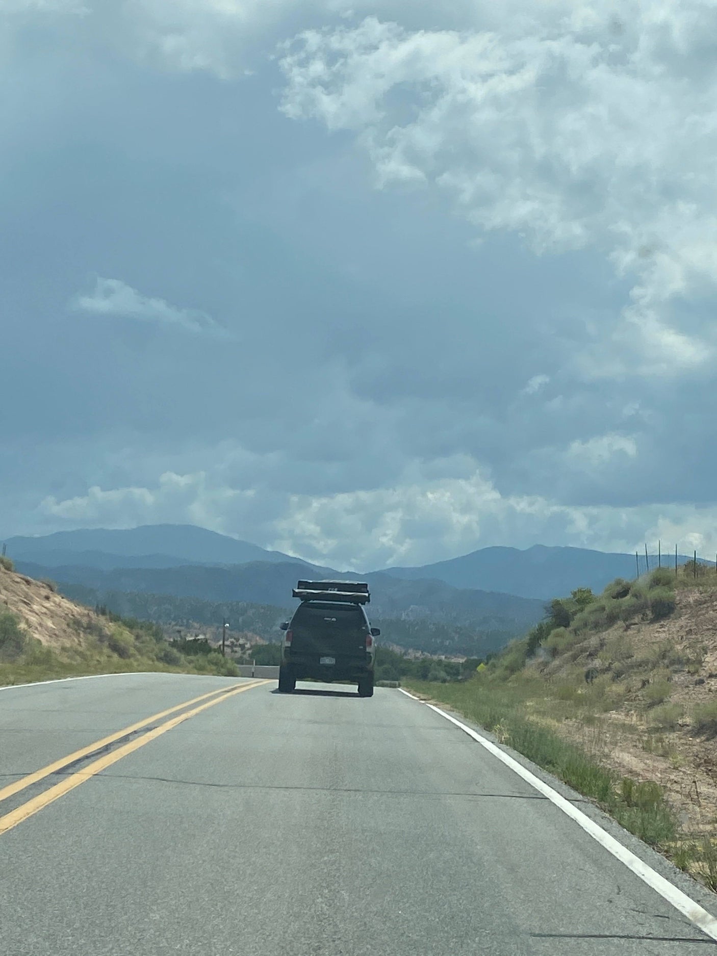 Black SUV with rooftop tent on a scenic mountain road under cloudy skies, ready for your RV rental adventure.