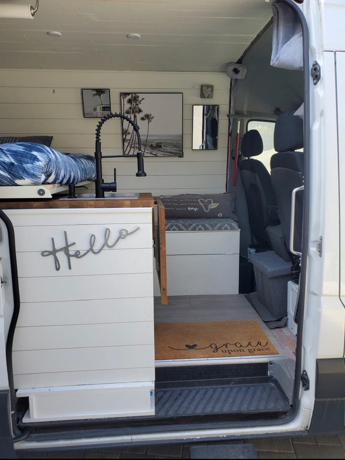 Step into this bright RV rental camper van, featuring a modern kitchen sink, comfy bed, and cozy seating area.
