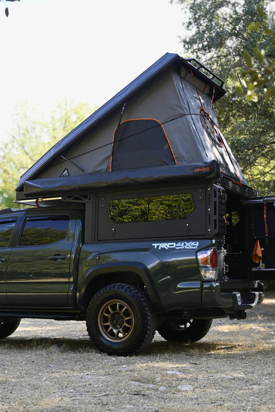 Green Toyota Tacoma truck with an open rooftop tent and camper shell. An ideal off-road rv rental for outdoor adventures.