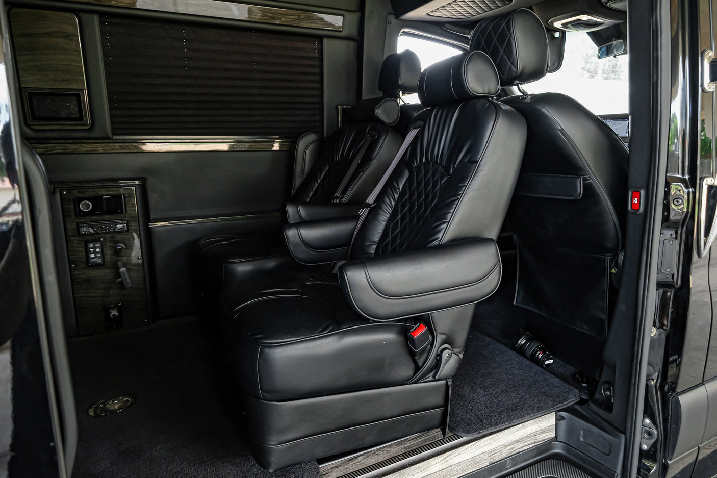 Inside a luxurious RV rental van: black leather captain's chairs, wood trim, and privacy blinds for ultimate comfort.