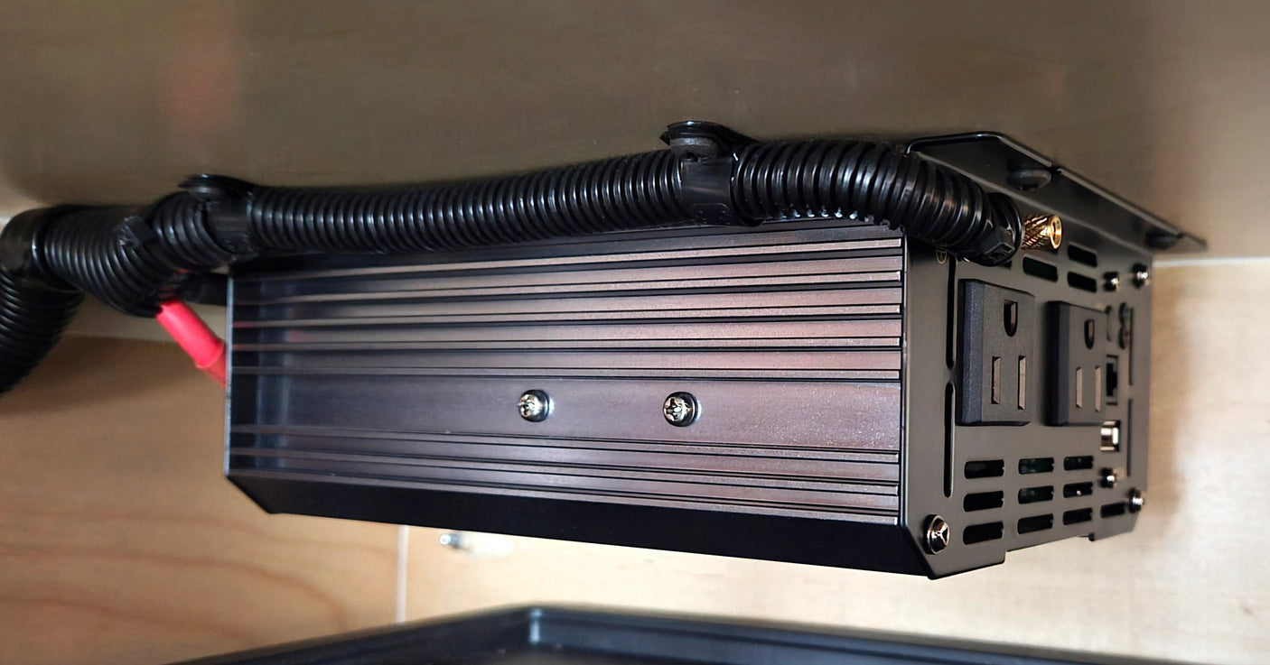 Power inverter, neatly wired under a shelf, providing outlets for RV rental electronics and reliable power connection.