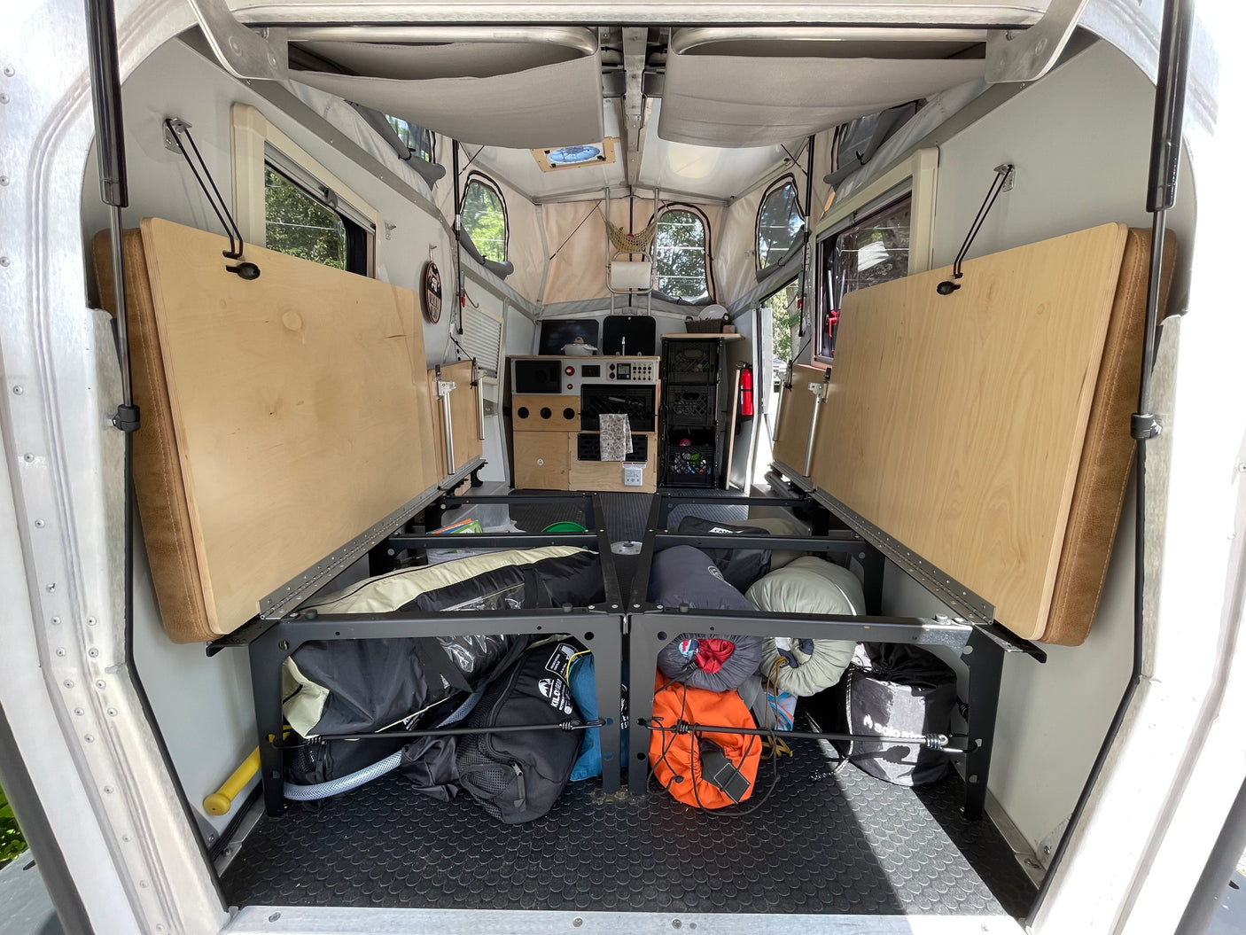 Interior of an RV rental: folded beds, under-bunk storage with gear, and a compact rear kitchen/control console.