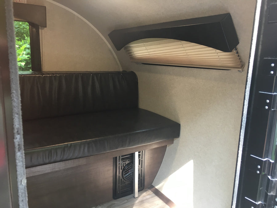 Interior of an RV rental showing a dark upholstered bench seat, side window, and pleated blinds over another window. A floor vent is visible.