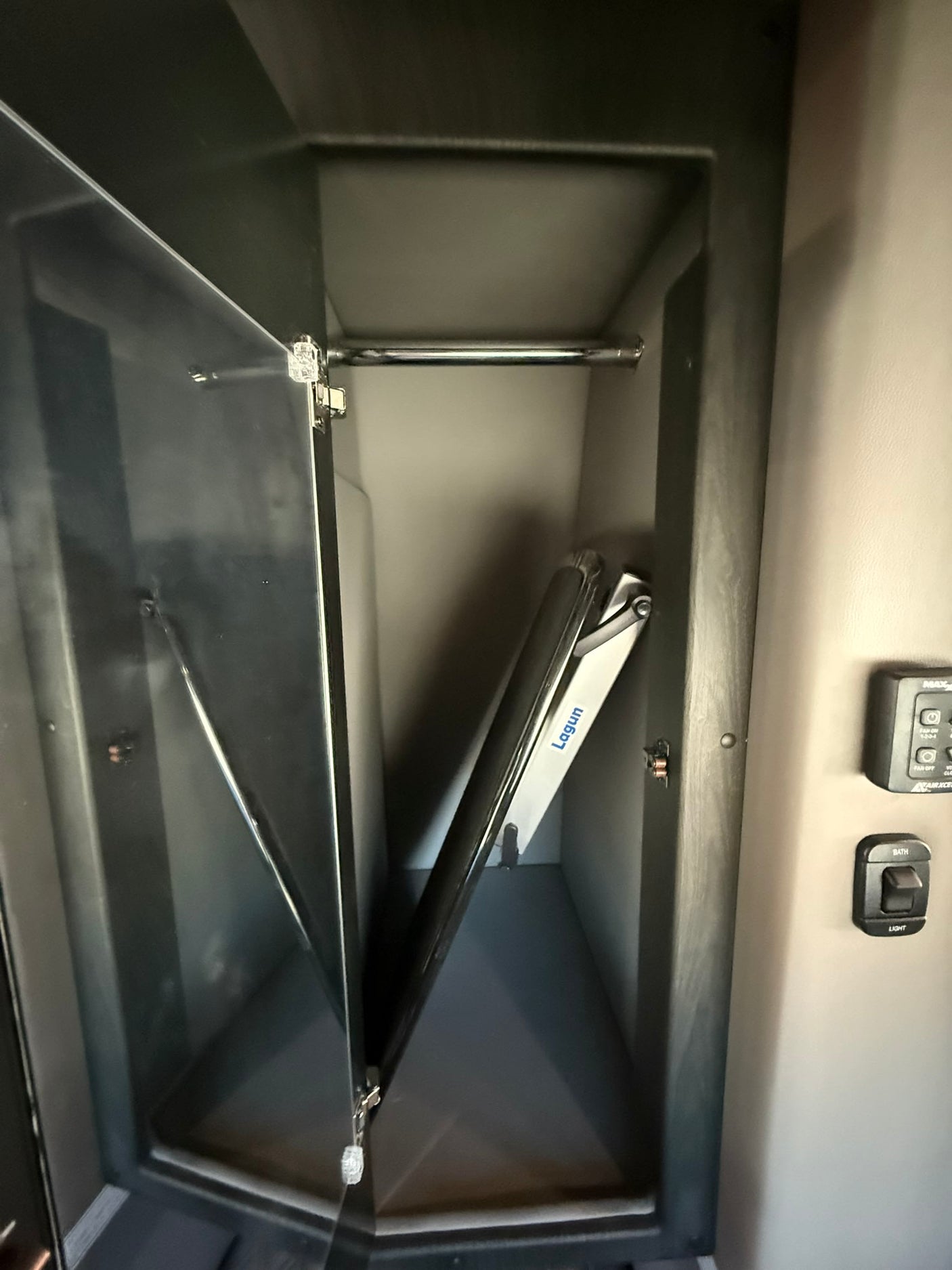 Inside this rv rental: an open camper closet with a hanging rod, folded Lagun table base, and adjacent light controls.