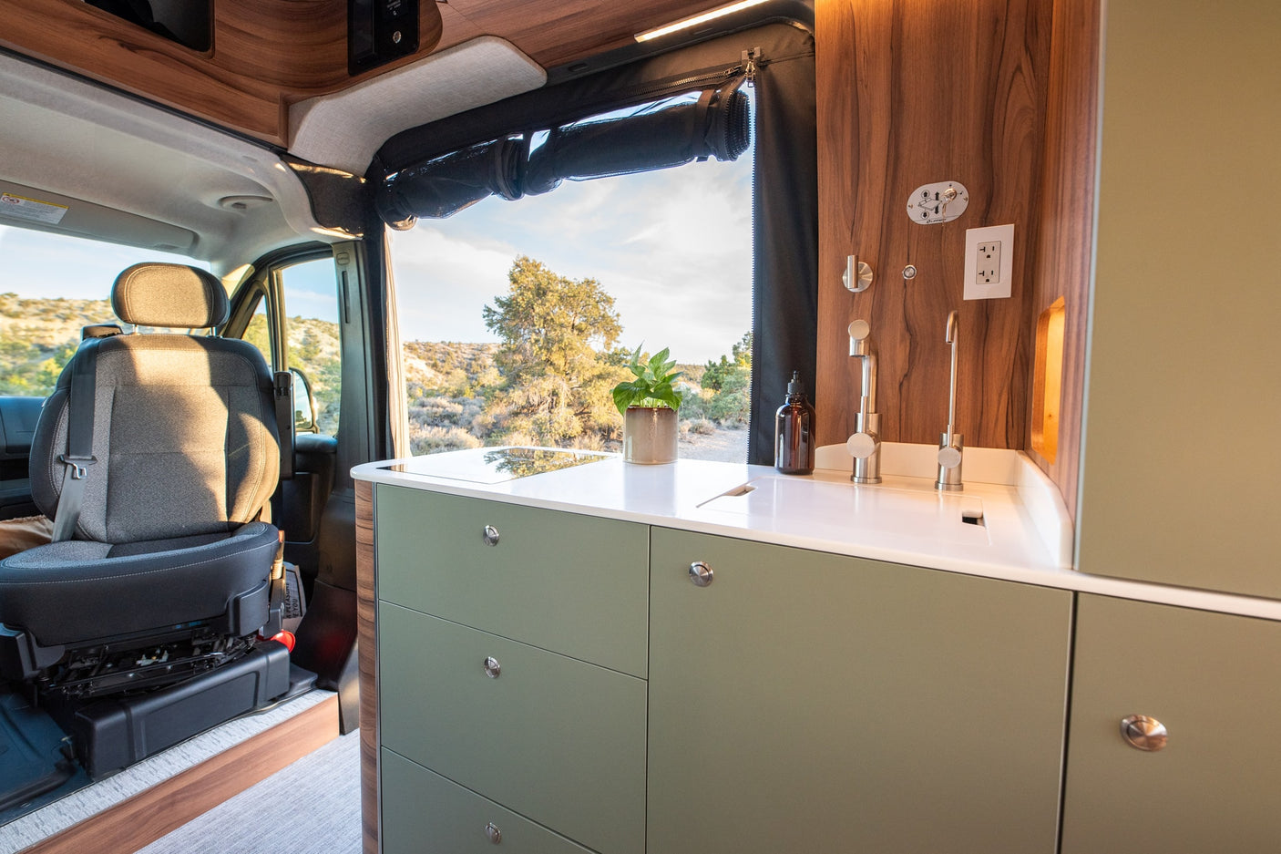 Stylish rv rental interior with a sage green kitchenette, wood accents, and a scenic outdoor view, perfect for road trips.
