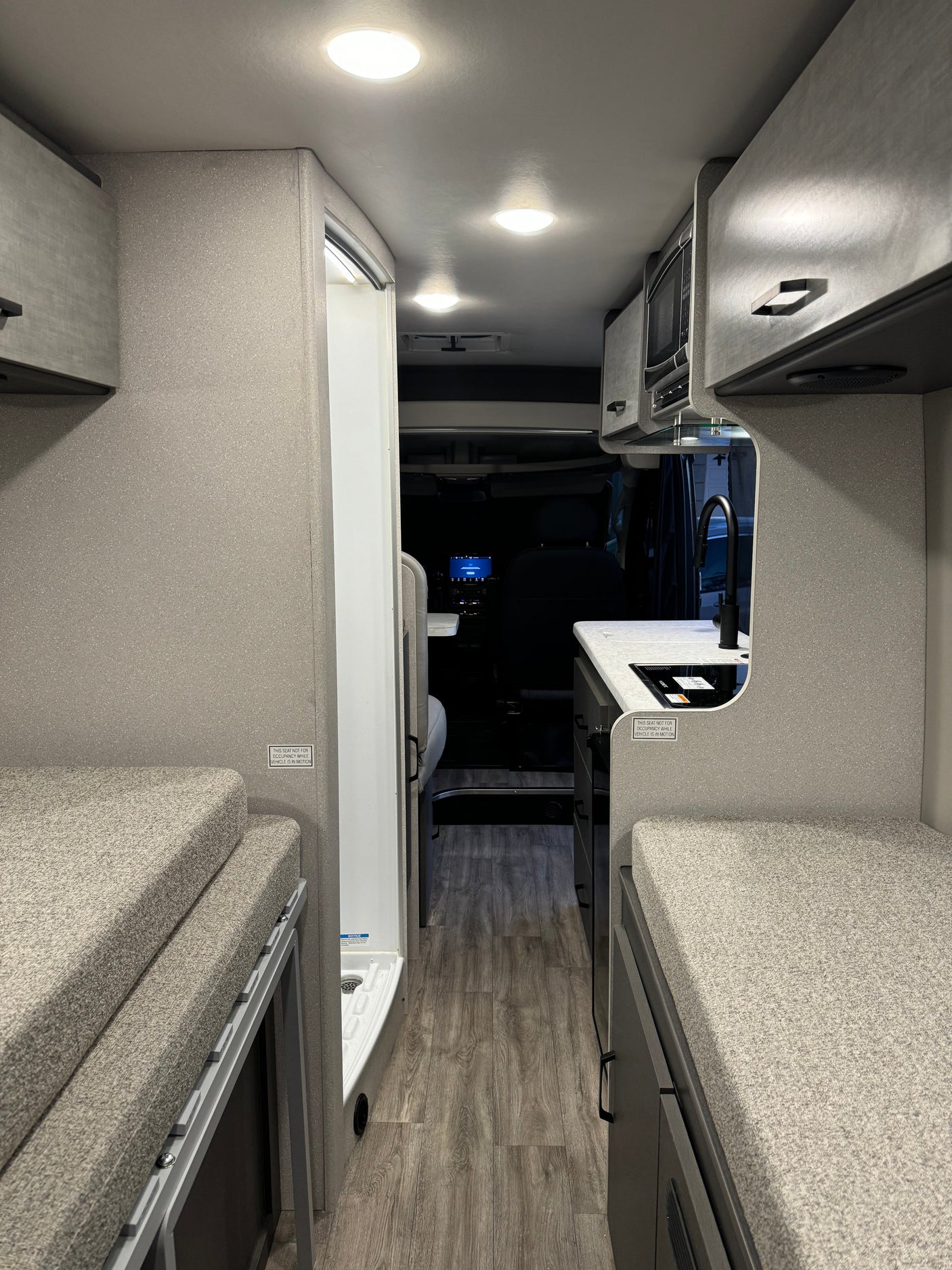 View inside a modern RV rental, showcasing its compact kitchen, shower, and convertible bench/bed spaces.