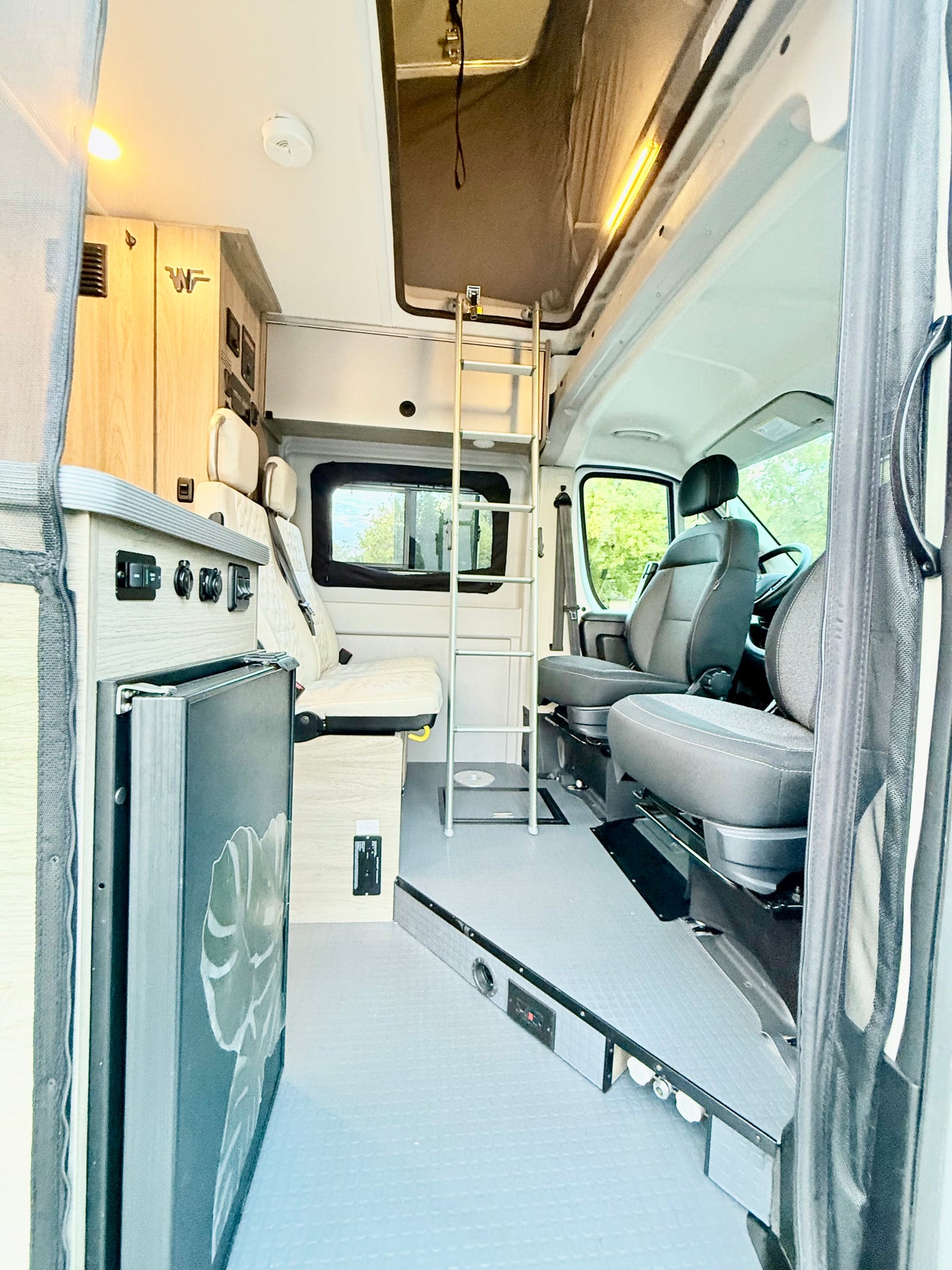 Explore this bright RV rental camper van interior: pop-top access via ladder, kitchenette, and comfortable front seats.