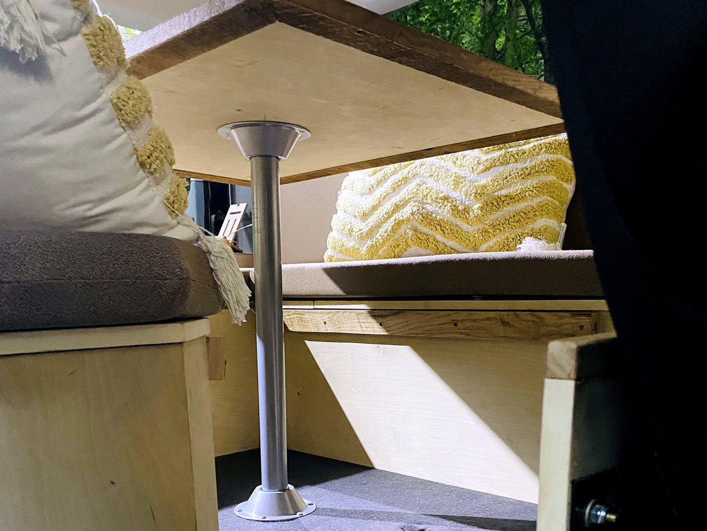 Inside an RV rental: a wooden table, cushioned benches with decorative pillows, with trees visible outside.
