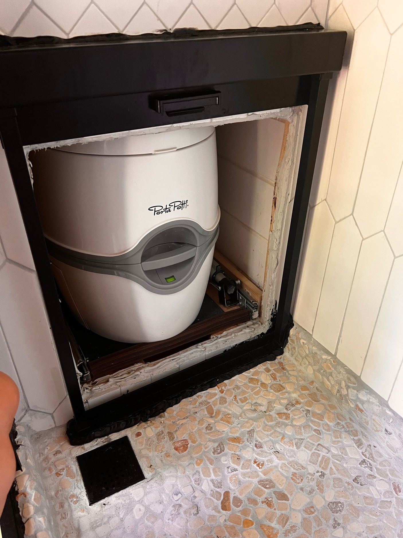 Porta Potti portable toilet neatly stored in a custom compartment, perfect for an RV rental or compact camper.