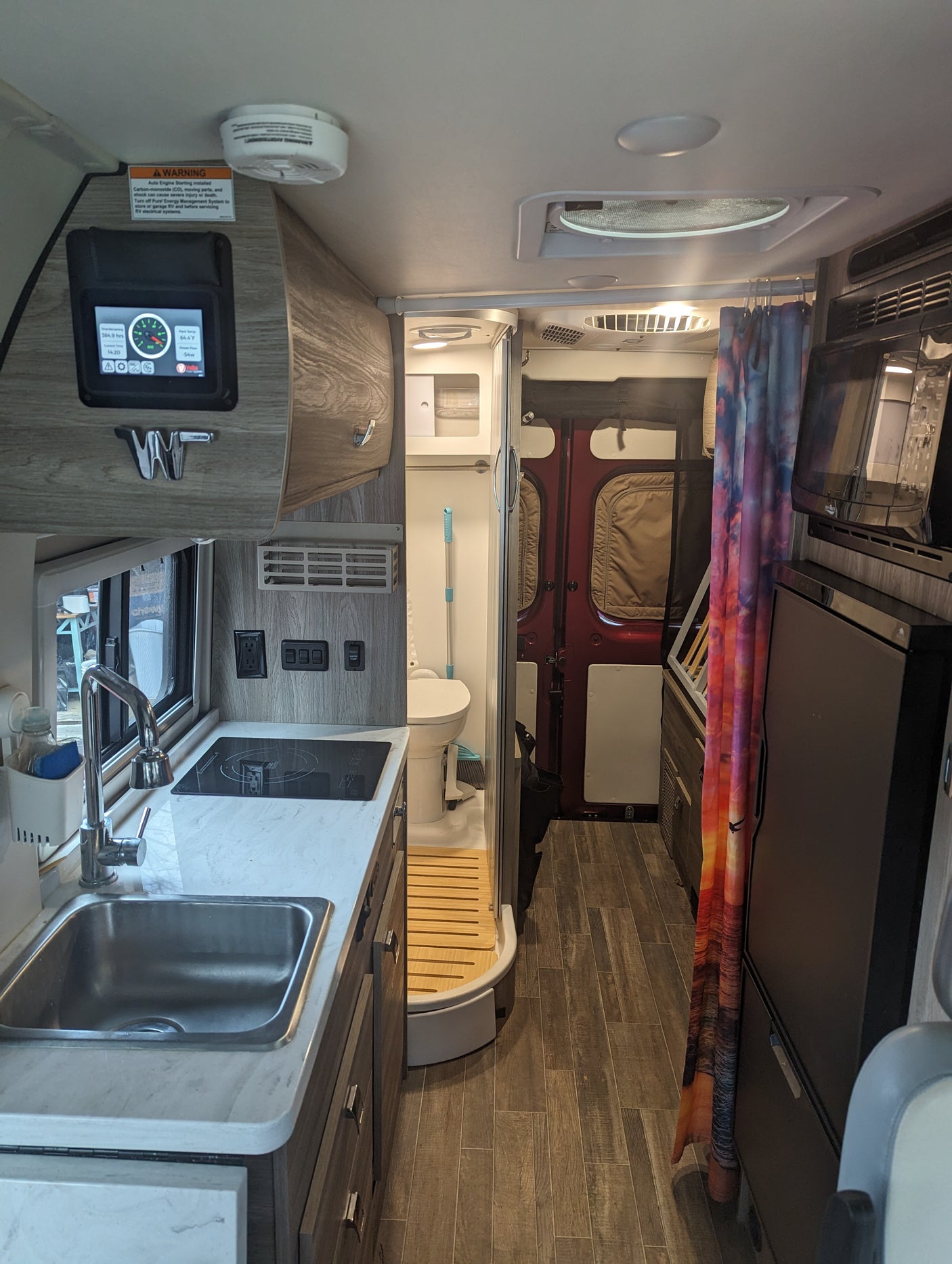This rv rental features a compact kitchen with a sink & cooktop, a bathroom, and a control panel for comfortable on-the-go living.