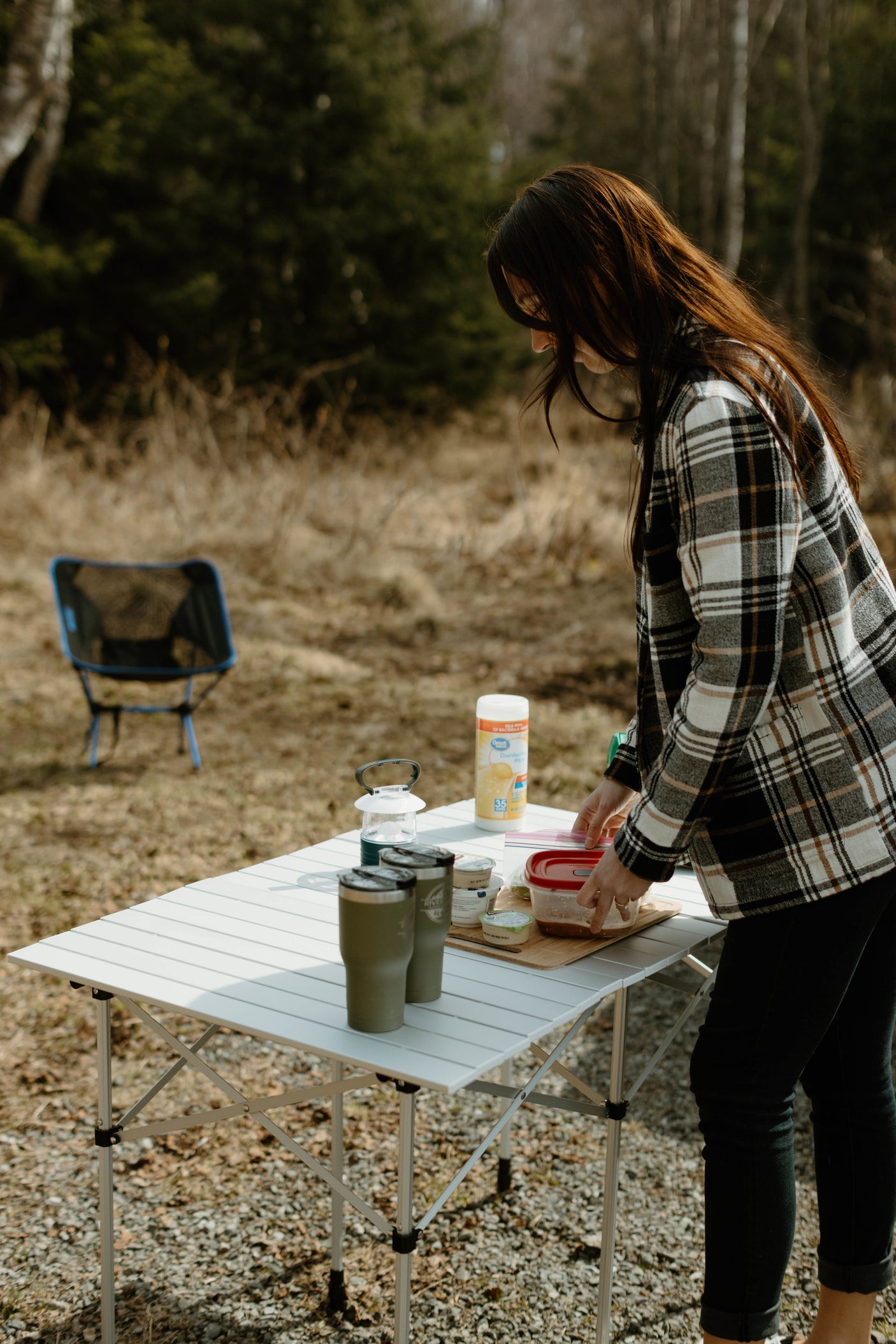 A woman sets up a portable camping table with food and supplies, ideal for an RV rental outdoor dining experience.