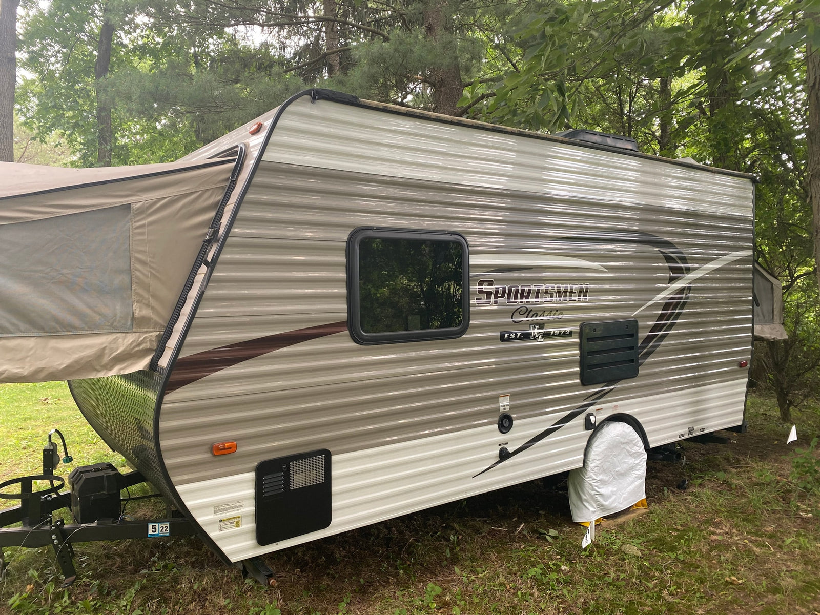 A beige pop-up hybrid travel trailer, an ideal rv rental for outdoor camping, is set up in a wooded site.