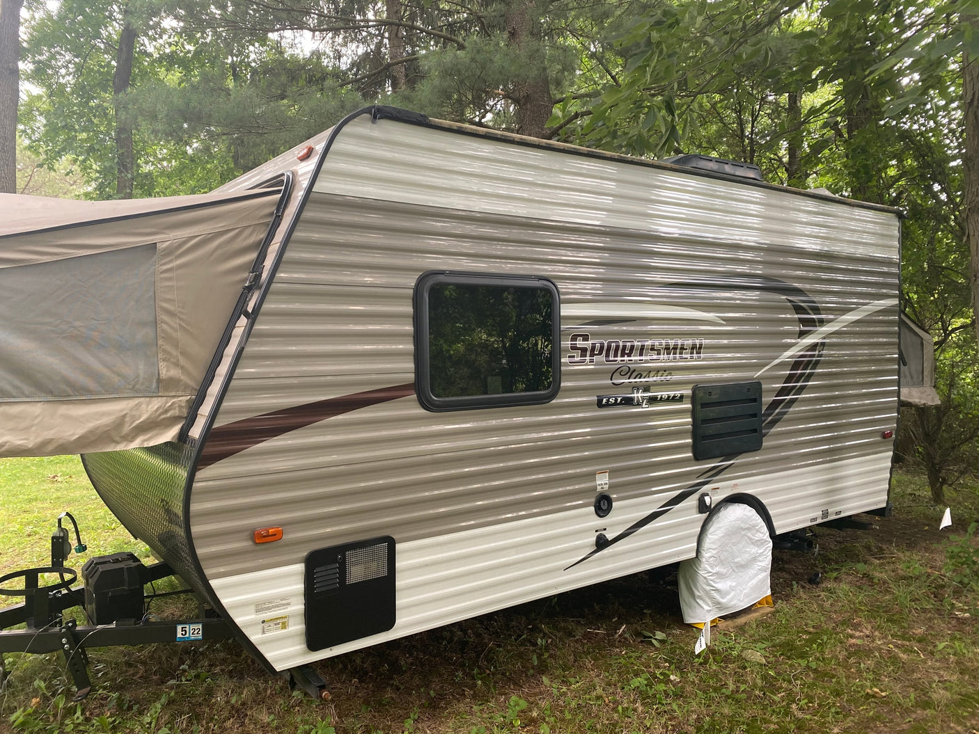 A beige pop-up hybrid travel trailer, an ideal rv rental for outdoor camping, is set up in a wooded site.