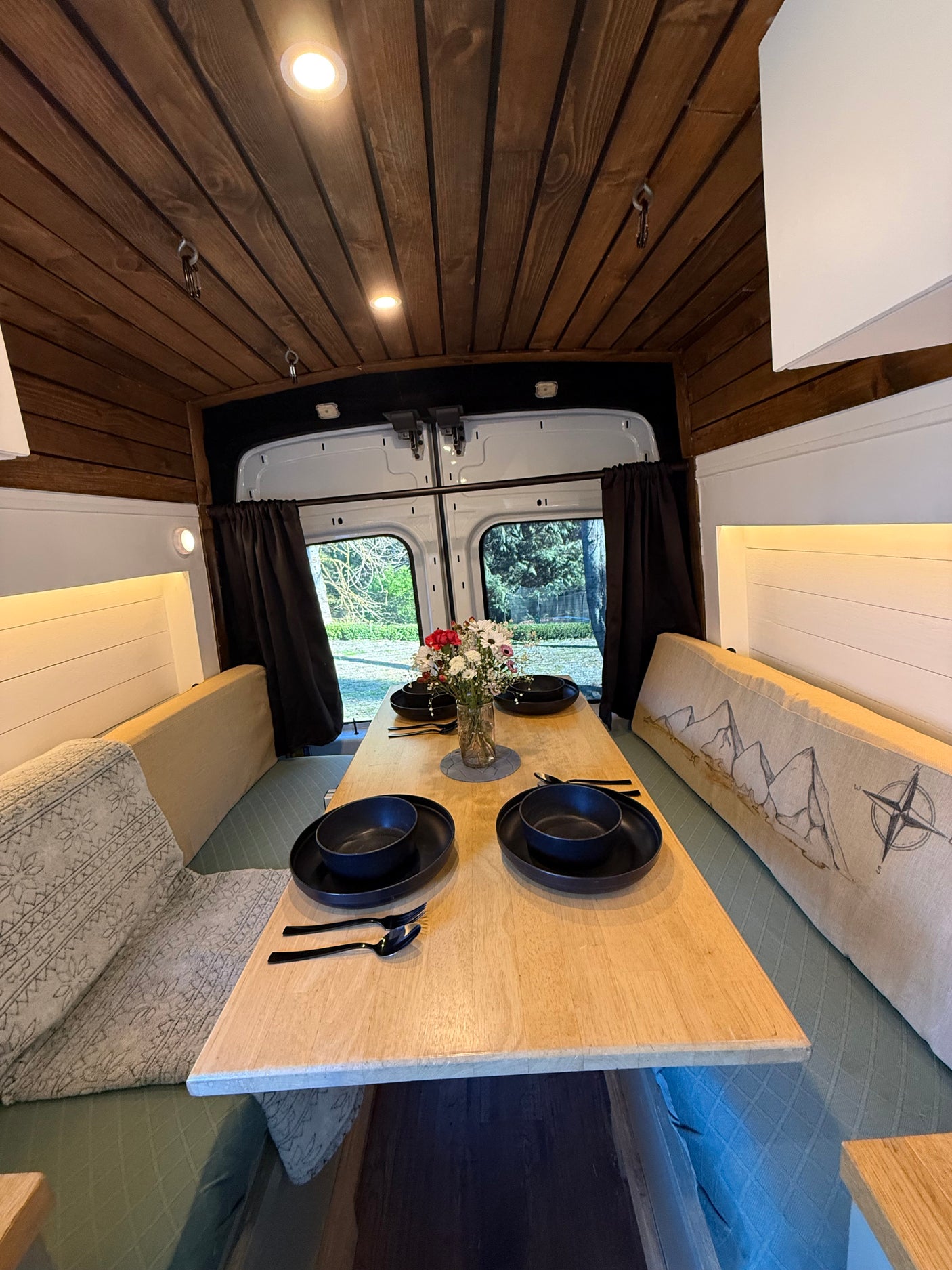 Cozy rv rental interior featuring a wooden dining table set for four, benches, and outdoor views.