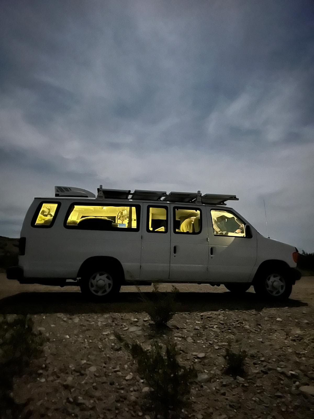 This Ford Econoline van, converted into a cozy RV rental, lights up the desert night. Solar-powered van life comfort.